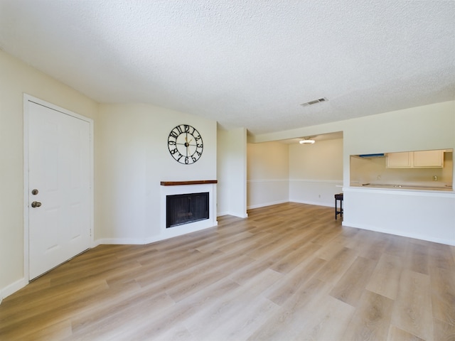 unfurnished living room with light wood-type flooring and a textured ceiling