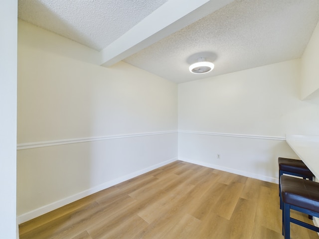 unfurnished room featuring beam ceiling, wood-type flooring, and a textured ceiling