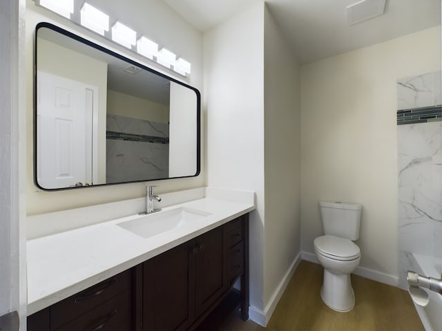 bathroom featuring toilet, wood-type flooring, vanity, and a tile shower