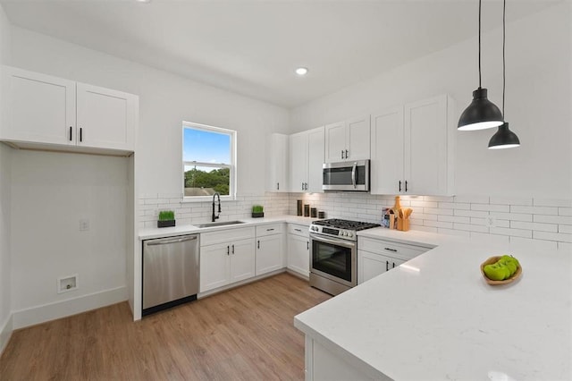 kitchen with stainless steel appliances, sink, white cabinets, light hardwood / wood-style floors, and hanging light fixtures