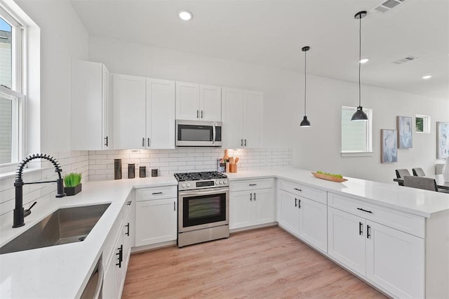 kitchen featuring pendant lighting, white cabinets, sink, kitchen peninsula, and stainless steel appliances