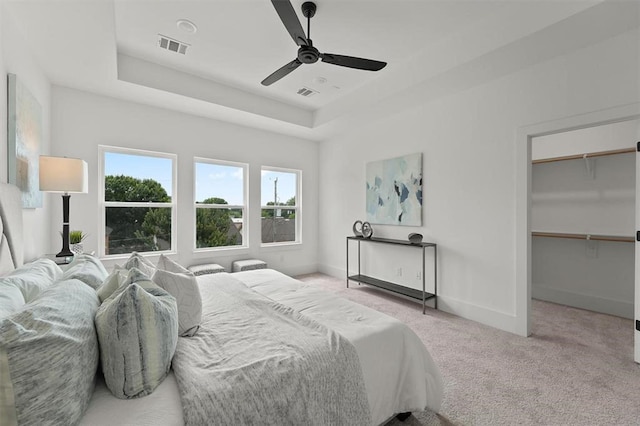 bedroom with light carpet, a raised ceiling, ceiling fan, a spacious closet, and a closet