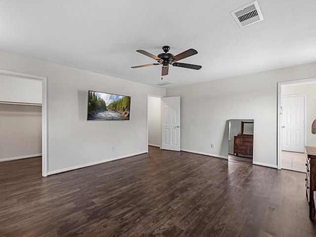 unfurnished bedroom featuring a closet, a walk in closet, dark hardwood / wood-style floors, and ceiling fan