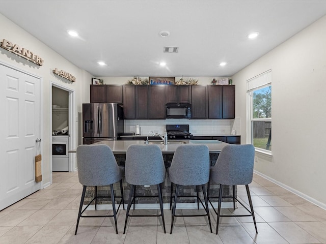 kitchen with black appliances, decorative backsplash, an island with sink, dark brown cabinetry, and a breakfast bar area