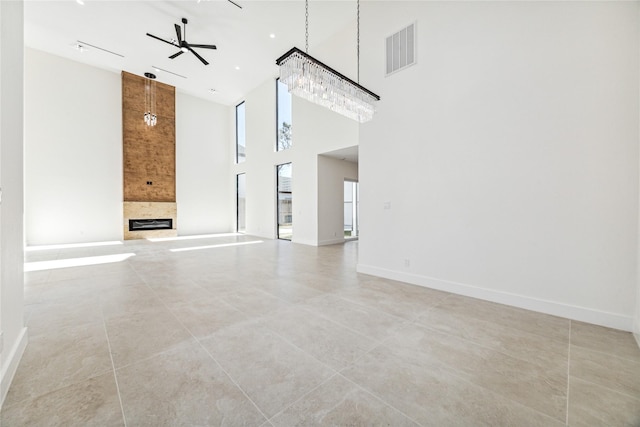 tiled empty room with ceiling fan with notable chandelier, a fireplace, and a high ceiling