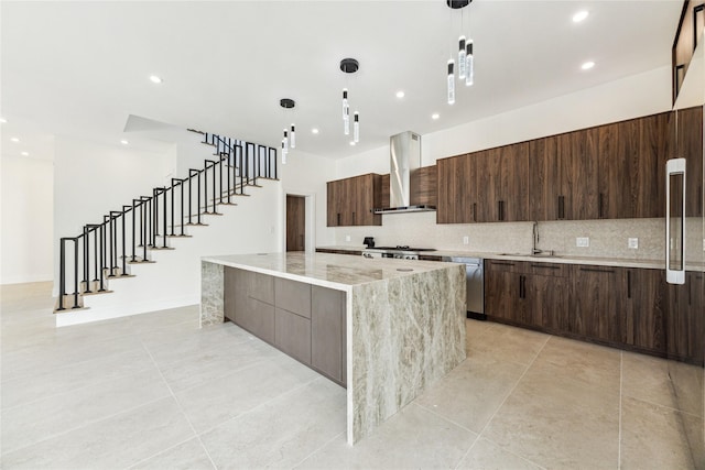 kitchen with pendant lighting, a spacious island, wall chimney range hood, sink, and tasteful backsplash