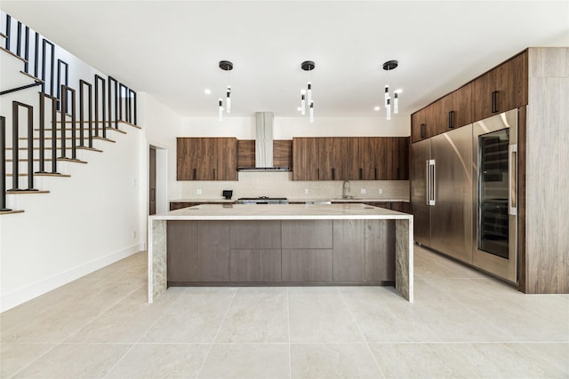 kitchen featuring pendant lighting, a center island, wall chimney exhaust hood, tasteful backsplash, and dark brown cabinetry