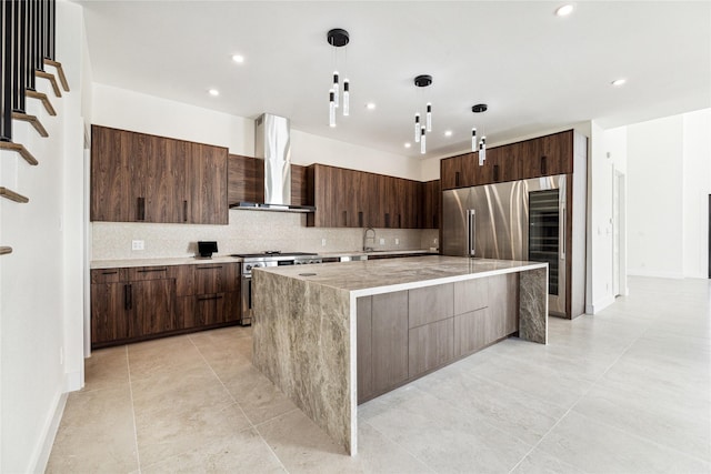 kitchen featuring a large island, wall chimney range hood, high end stove, pendant lighting, and decorative backsplash