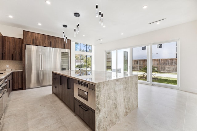 kitchen featuring hanging light fixtures, light stone counters, backsplash, a kitchen island, and appliances with stainless steel finishes