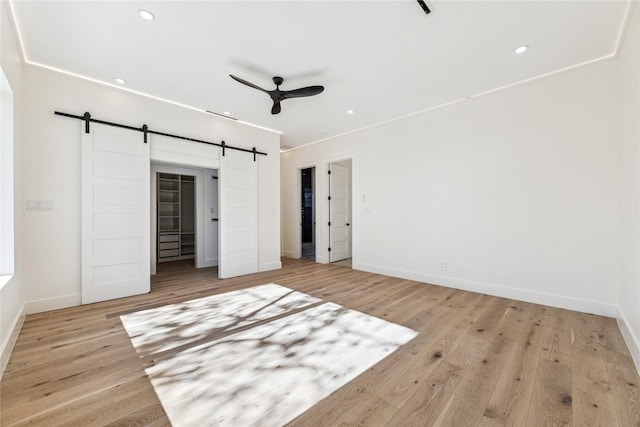 unfurnished bedroom featuring ceiling fan, a barn door, and light wood-type flooring