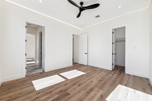 unfurnished bedroom featuring a walk in closet, ensuite bath, ceiling fan, light hardwood / wood-style flooring, and a closet