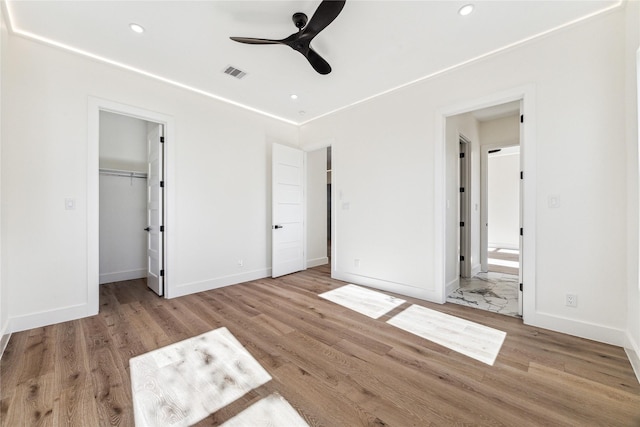 unfurnished bedroom featuring a walk in closet, ensuite bath, ceiling fan, light hardwood / wood-style floors, and a closet