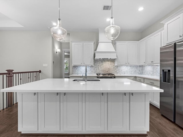 kitchen with a kitchen island with sink, dark wood-type flooring, stainless steel appliances, and decorative light fixtures