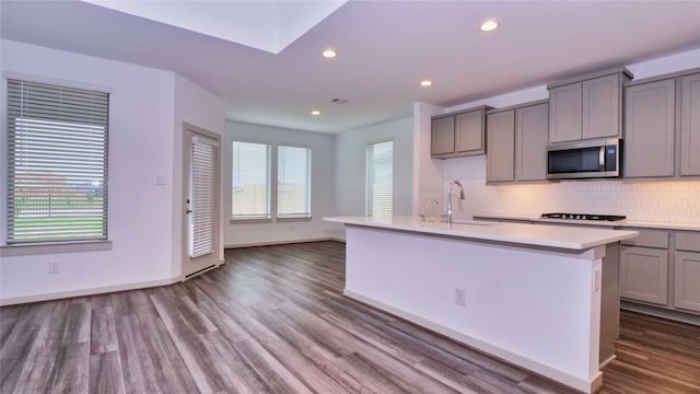 kitchen with gray cabinetry, sink, tasteful backsplash, wood-type flooring, and a center island with sink