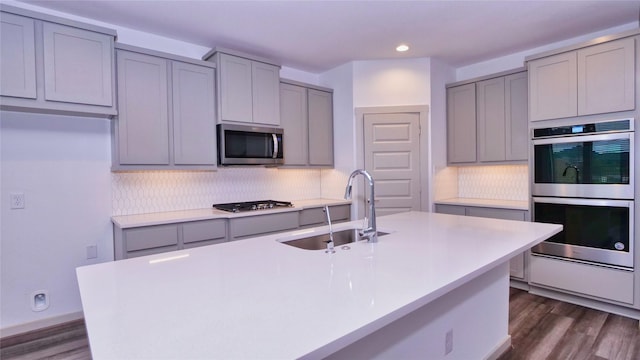 kitchen featuring dark hardwood / wood-style flooring, stainless steel appliances, sink, gray cabinets, and an island with sink