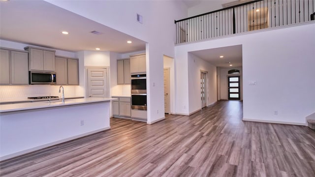 kitchen with appliances with stainless steel finishes, a towering ceiling, sink, light hardwood / wood-style flooring, and gray cabinets