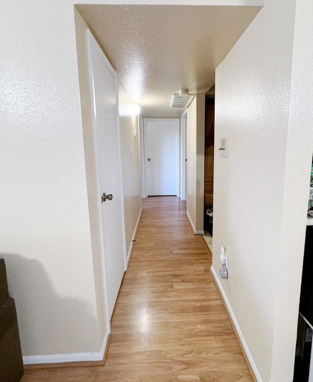 hall featuring a textured ceiling and light hardwood / wood-style flooring