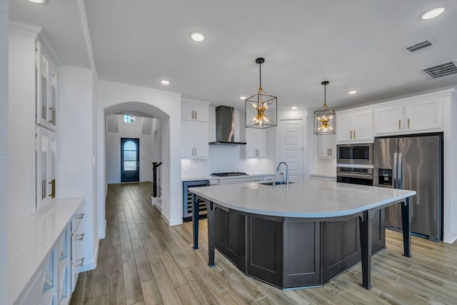 kitchen with appliances with stainless steel finishes, beverage cooler, pendant lighting, wall chimney exhaust hood, and white cabinets