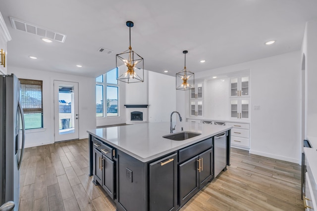 kitchen with decorative light fixtures, sink, light hardwood / wood-style flooring, a kitchen island with sink, and appliances with stainless steel finishes