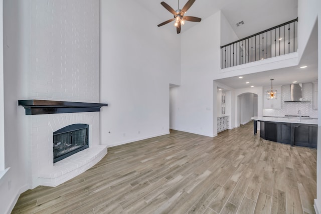 unfurnished living room featuring a high ceiling, a fireplace, sink, light wood-type flooring, and ceiling fan