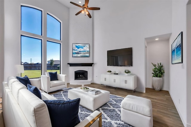 living room with ceiling fan, a fireplace, a high ceiling, and hardwood / wood-style flooring