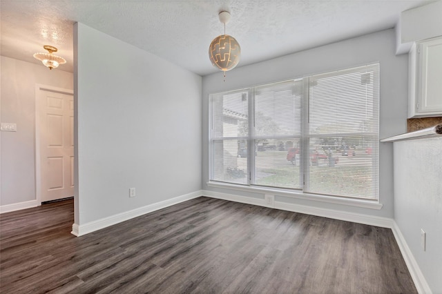 unfurnished dining area with dark wood finished floors, a textured ceiling, and baseboards