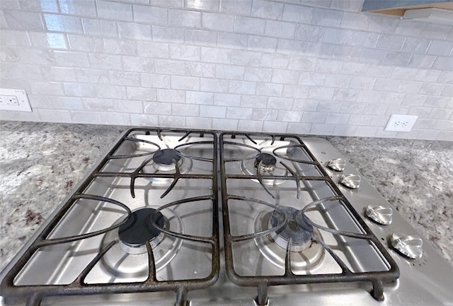 details with stainless steel stovetop, decorative backsplash, and light stone countertops