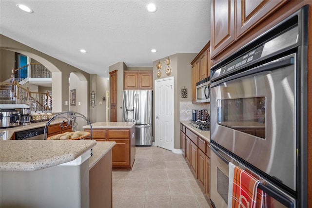 kitchen with decorative backsplash, appliances with stainless steel finishes, a textured ceiling, a center island, and light tile patterned flooring