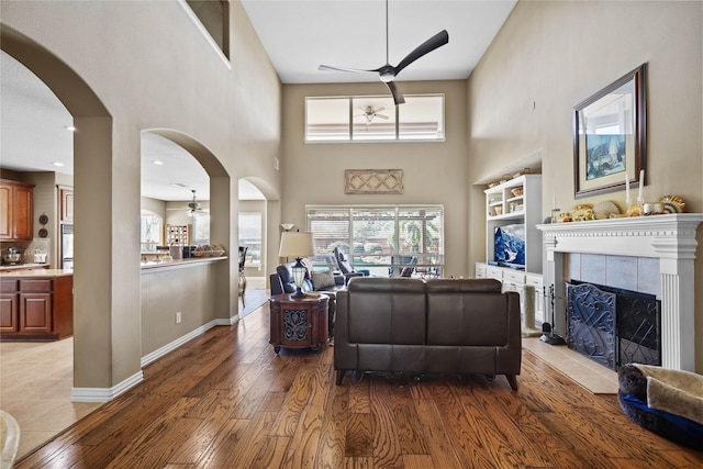 living room featuring a tiled fireplace, ceiling fan, wood-type flooring, and a high ceiling