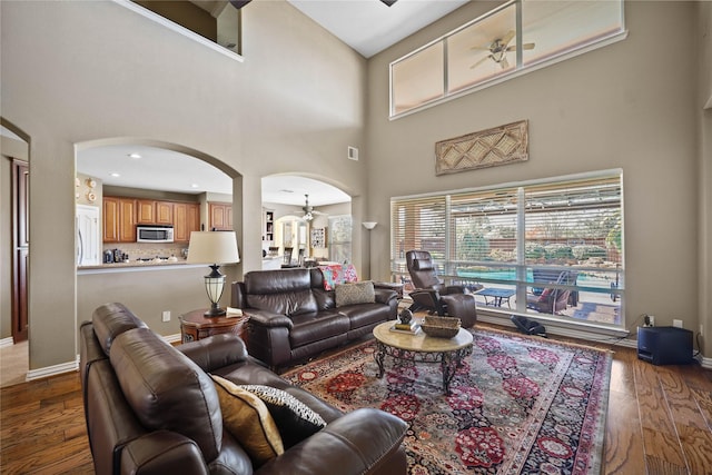 living room with ceiling fan with notable chandelier, a towering ceiling, and dark hardwood / wood-style floors