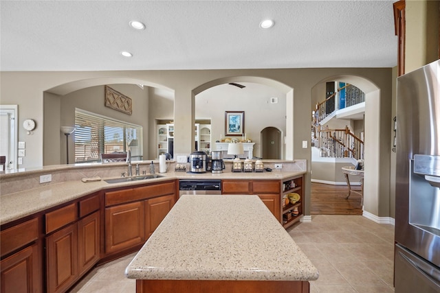 kitchen with sink, light stone counters, a textured ceiling, a kitchen island, and appliances with stainless steel finishes