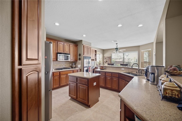 kitchen with sink, ceiling fan, a textured ceiling, a kitchen island, and stainless steel appliances