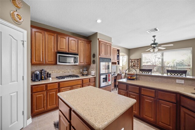 kitchen featuring tasteful backsplash, light tile patterned flooring, a textured ceiling, a kitchen island, and appliances with stainless steel finishes