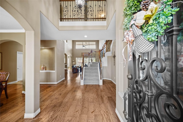 entryway with wood-type flooring, crown molding, and a towering ceiling