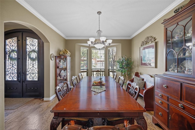 dining area featuring an inviting chandelier, crown molding, light hardwood / wood-style flooring, and french doors