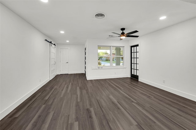 unfurnished living room with a barn door, ceiling fan, and dark wood-type flooring