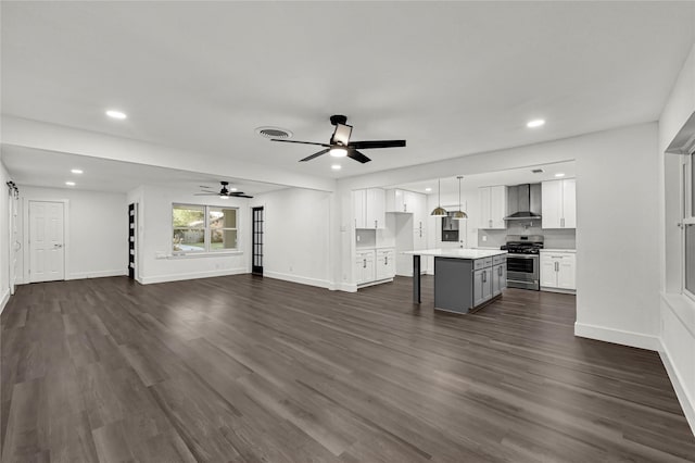 kitchen featuring dark hardwood / wood-style flooring, stainless steel gas range, wall chimney range hood, a center island, and white cabinetry