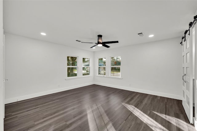 empty room featuring ceiling fan, a barn door, and dark wood-type flooring