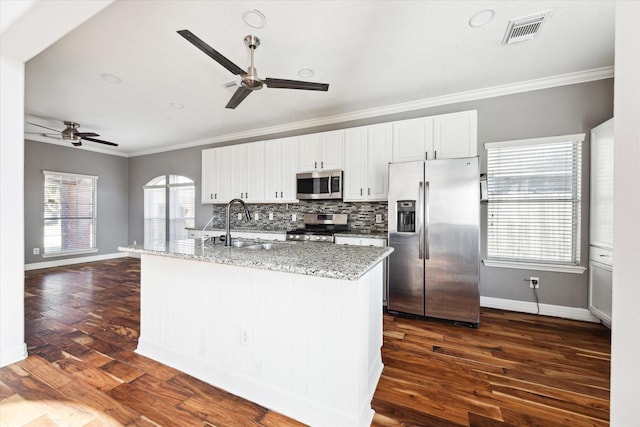 kitchen with dark hardwood / wood-style floors, ornamental molding, an island with sink, and appliances with stainless steel finishes