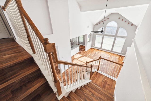 stairs with ceiling fan, high vaulted ceiling, and hardwood / wood-style flooring