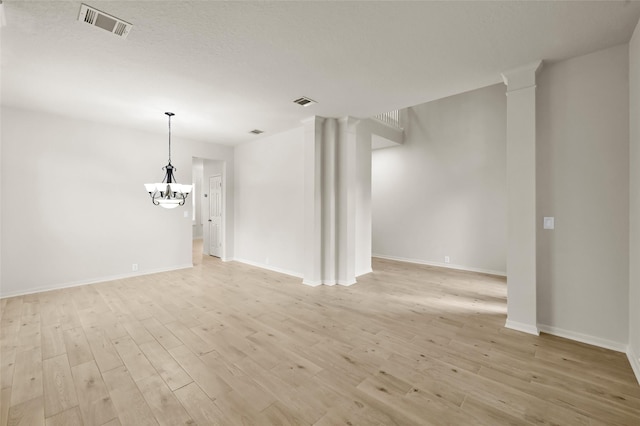 spare room with a chandelier, a textured ceiling, and light hardwood / wood-style floors