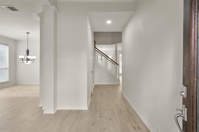 hallway featuring an inviting chandelier, light hardwood / wood-style flooring, and ornate columns