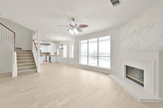 unfurnished living room featuring ceiling fan with notable chandelier, a fireplace, and light hardwood / wood-style floors