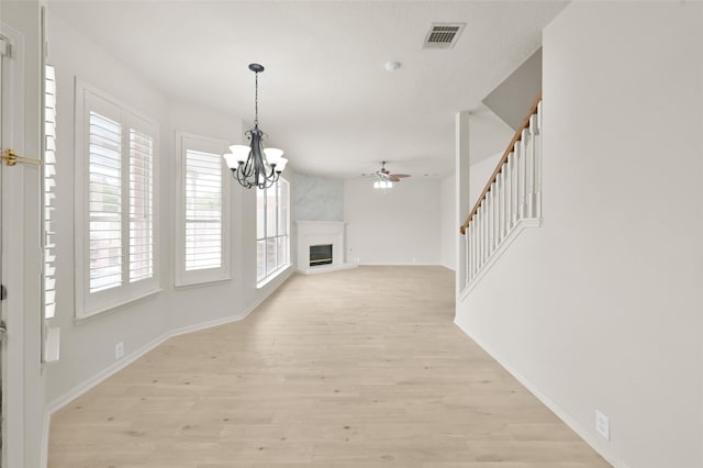 unfurnished living room with ceiling fan with notable chandelier, a fireplace, and light hardwood / wood-style floors