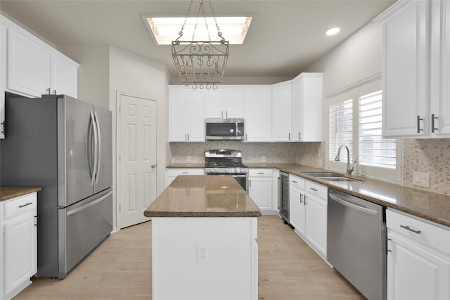 kitchen featuring sink, appliances with stainless steel finishes, white cabinets, a kitchen island, and dark stone counters