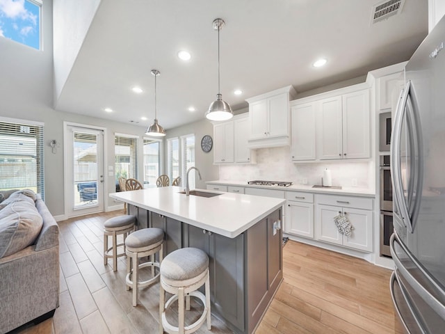 kitchen with white cabinetry, sink, stainless steel appliances, light hardwood / wood-style flooring, and decorative light fixtures