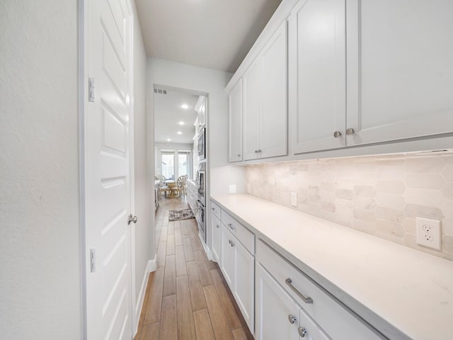 kitchen featuring tasteful backsplash, stainless steel oven, light hardwood / wood-style flooring, and white cabinets