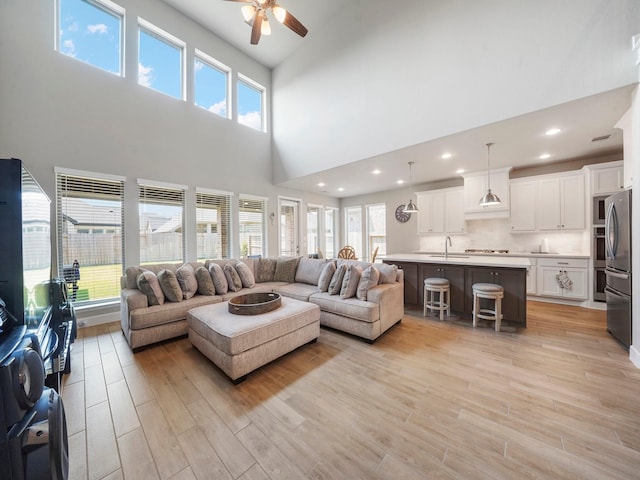 living room with ceiling fan, light hardwood / wood-style floors, sink, and a high ceiling