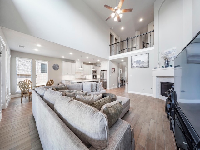 living room featuring ceiling fan, sink, high vaulted ceiling, and light wood-type flooring