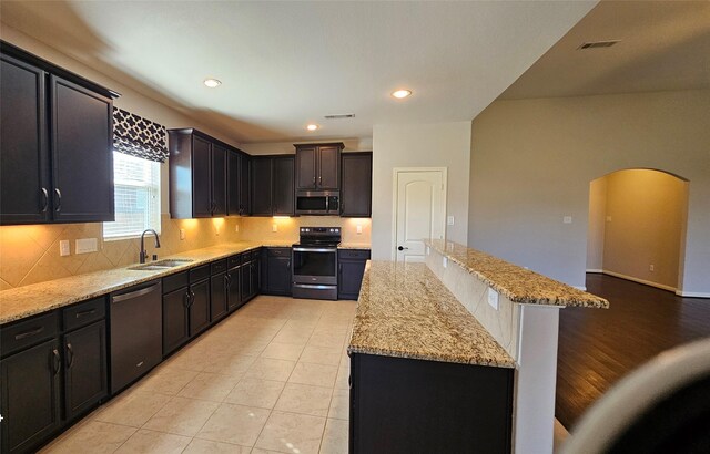 kitchen with a kitchen island, a breakfast bar, sink, stainless steel appliances, and light stone counters